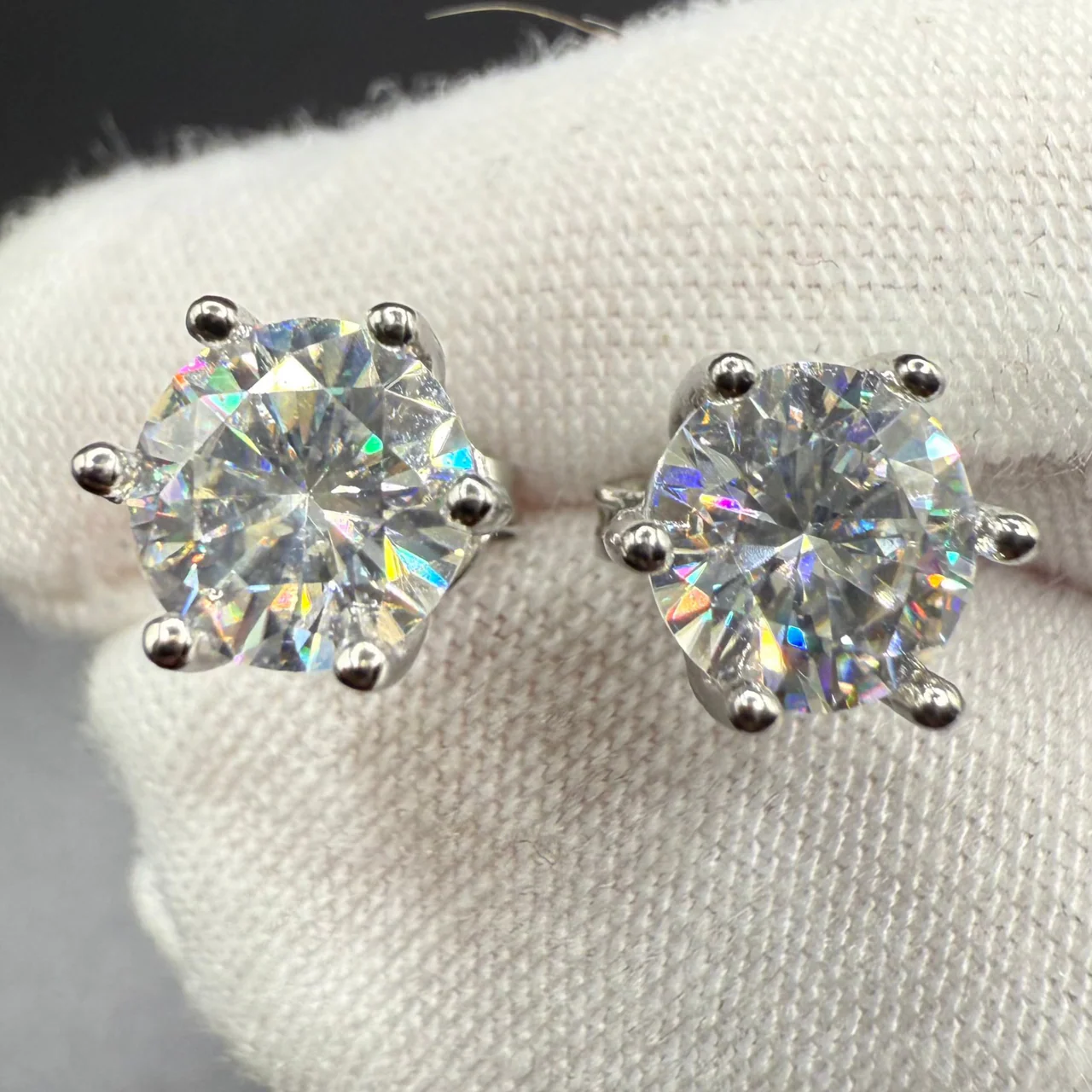 Round brilliant moissanite stud earrings held in a gloved hand